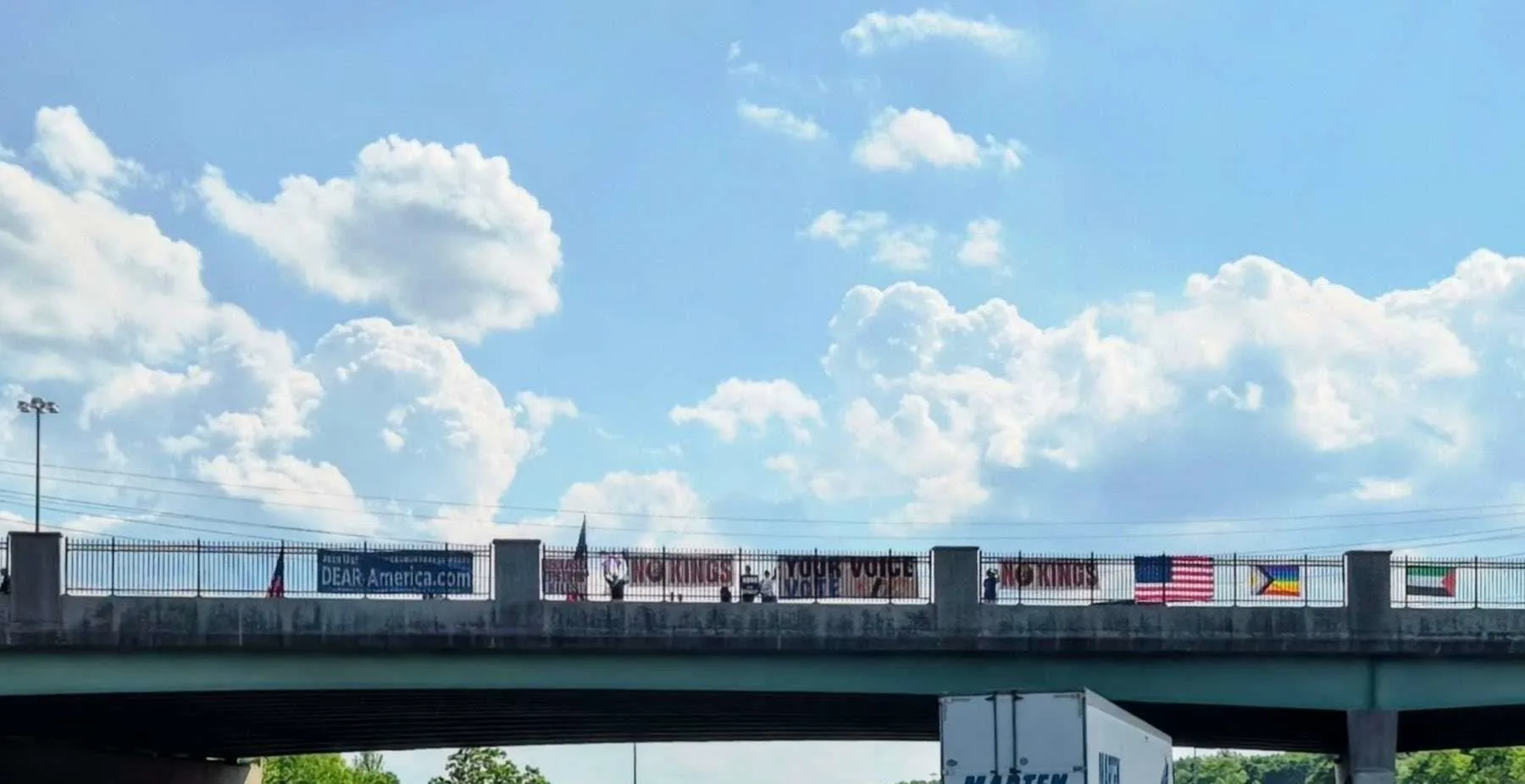 DEAR America members on a highway overpass with No Kings banners, flags, and Your Voice Your Vote signs.